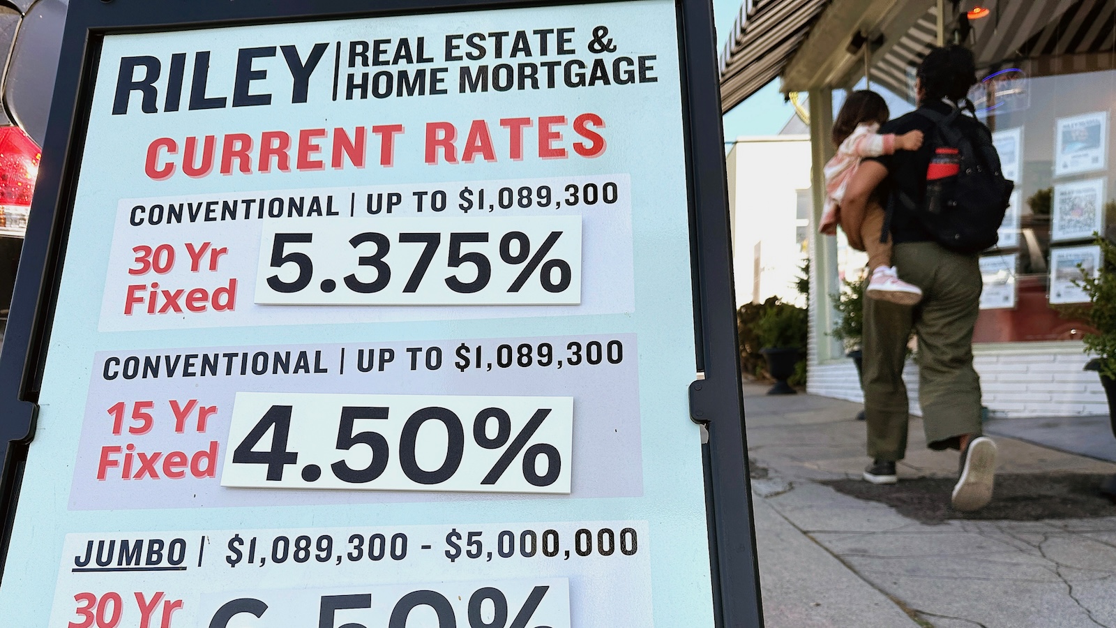 Pedestrians walk by a sidewalk sandwich board providing the latest interest rates for home mortgages.