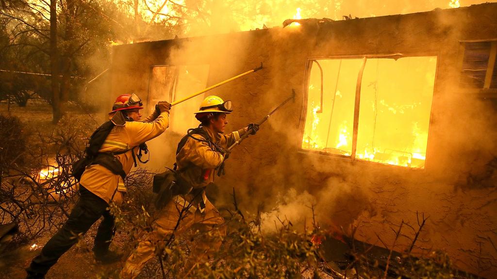 Firefighters try to keep flames from burning home from spreading to a neighboring apartment complex as they battle the Camp Fire on November 9, 2018 in Paradise, California.