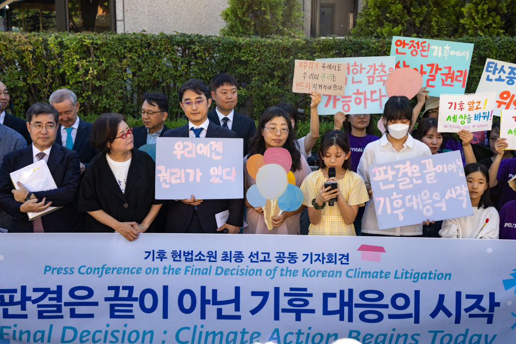 Korean plaintiffs holding placards stand before sign