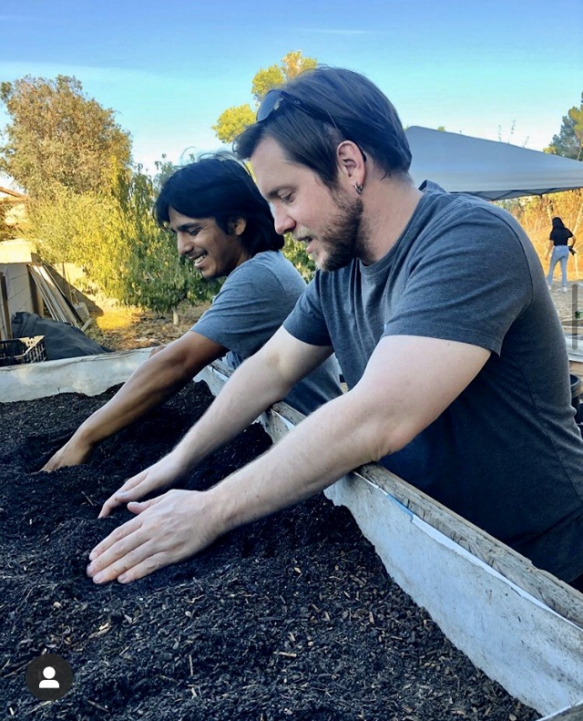 Two men with hands in compost heap