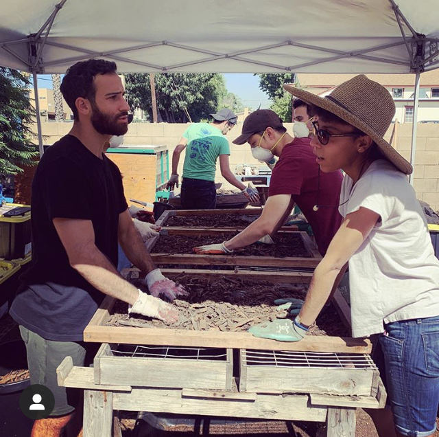 Two people stand with hands in compost