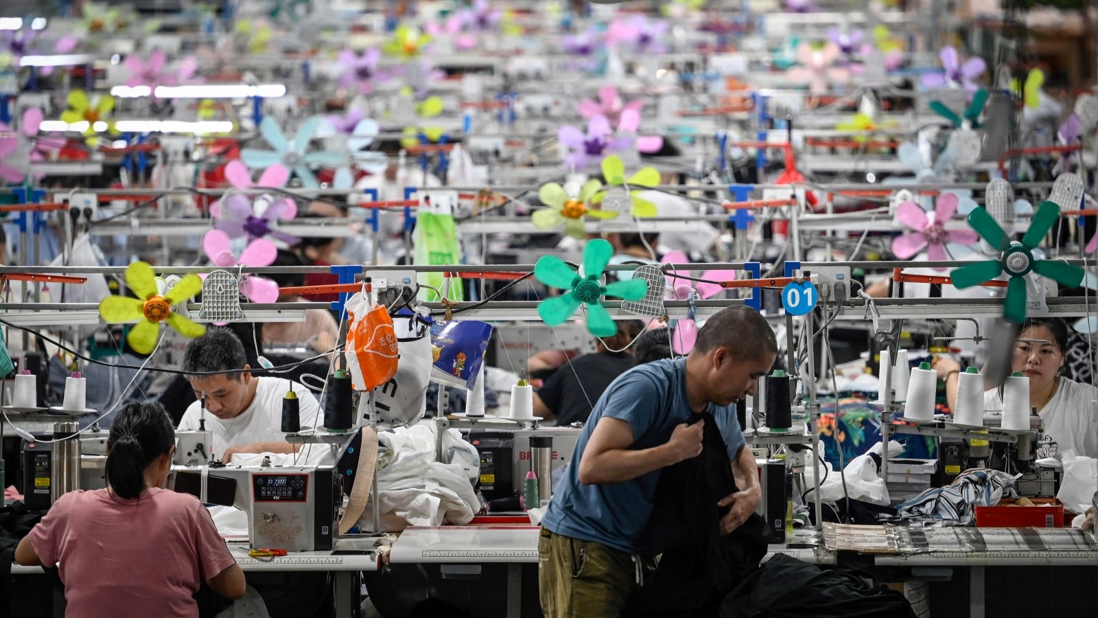 Many colorful rows of tightly packed sewing machines and workers at a factory.