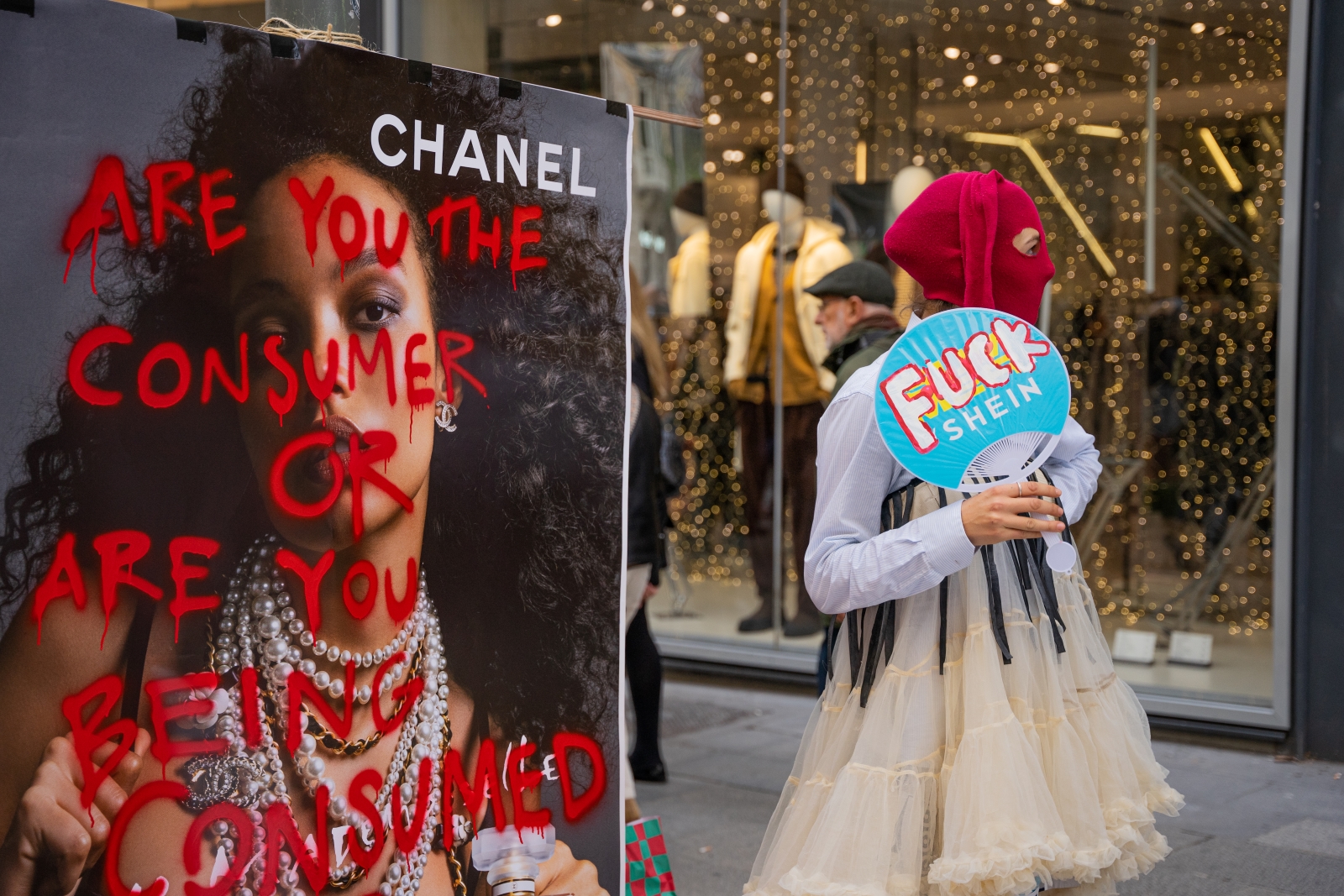 企業網站 A person in a tutu and red balaclava holds a Shein-branded fan that has been painted over to say 