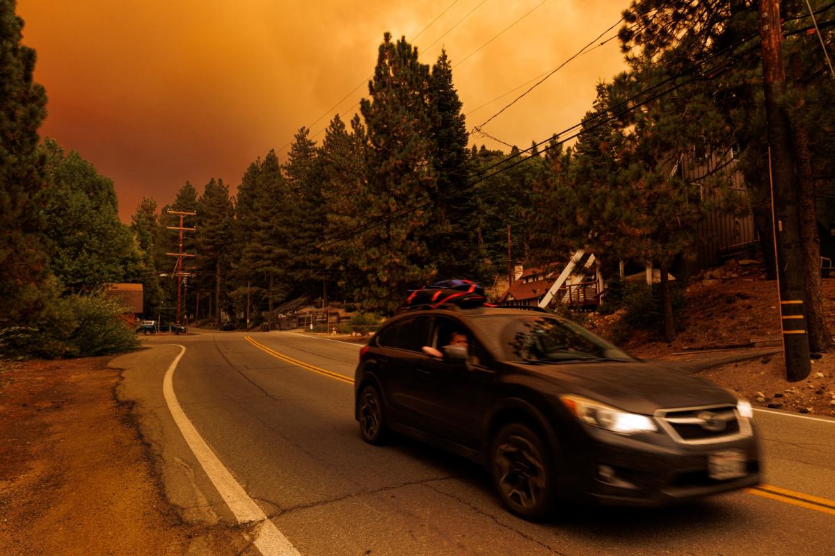 A car races ahead of a wildfire, with orange, smoky skies in the background