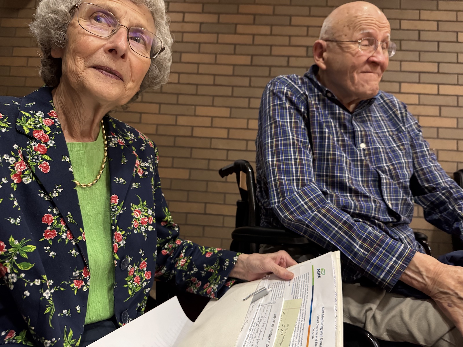 A woman holds a folder of papers seated next to an elderly man