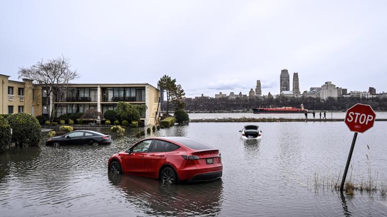 A red Tesla Model Y is partially submerged in the flooded parking lot of an apartment building.