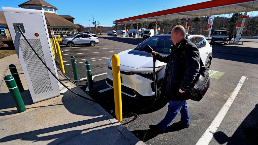 A middle-aged man prepares to plug his electric vehicle into a public charger at a filling station on the Massachusetts Turnpike.