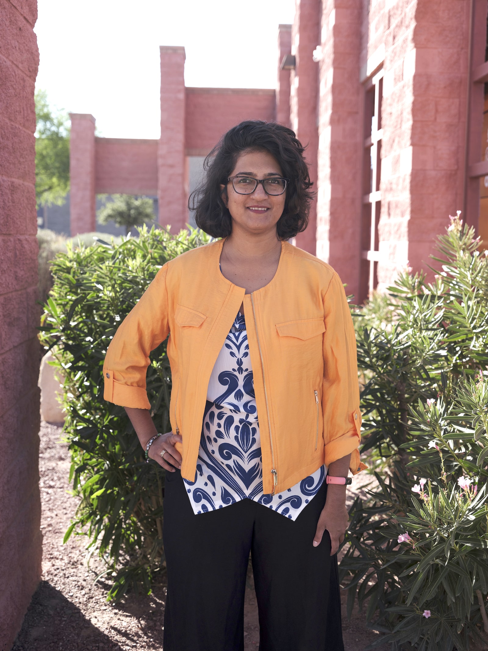 A woman in a yellow cardigan poses in front of terracotta-color buildings