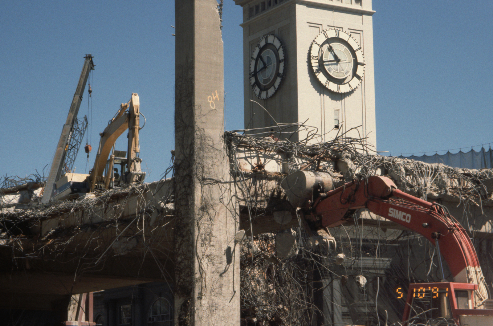 a partially dismantled freeway and clock tower with construction equipment