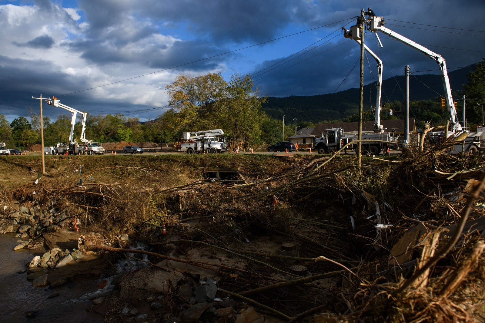 Line workers repair power lines against a scene of hurricane damage, with downed trees and debris