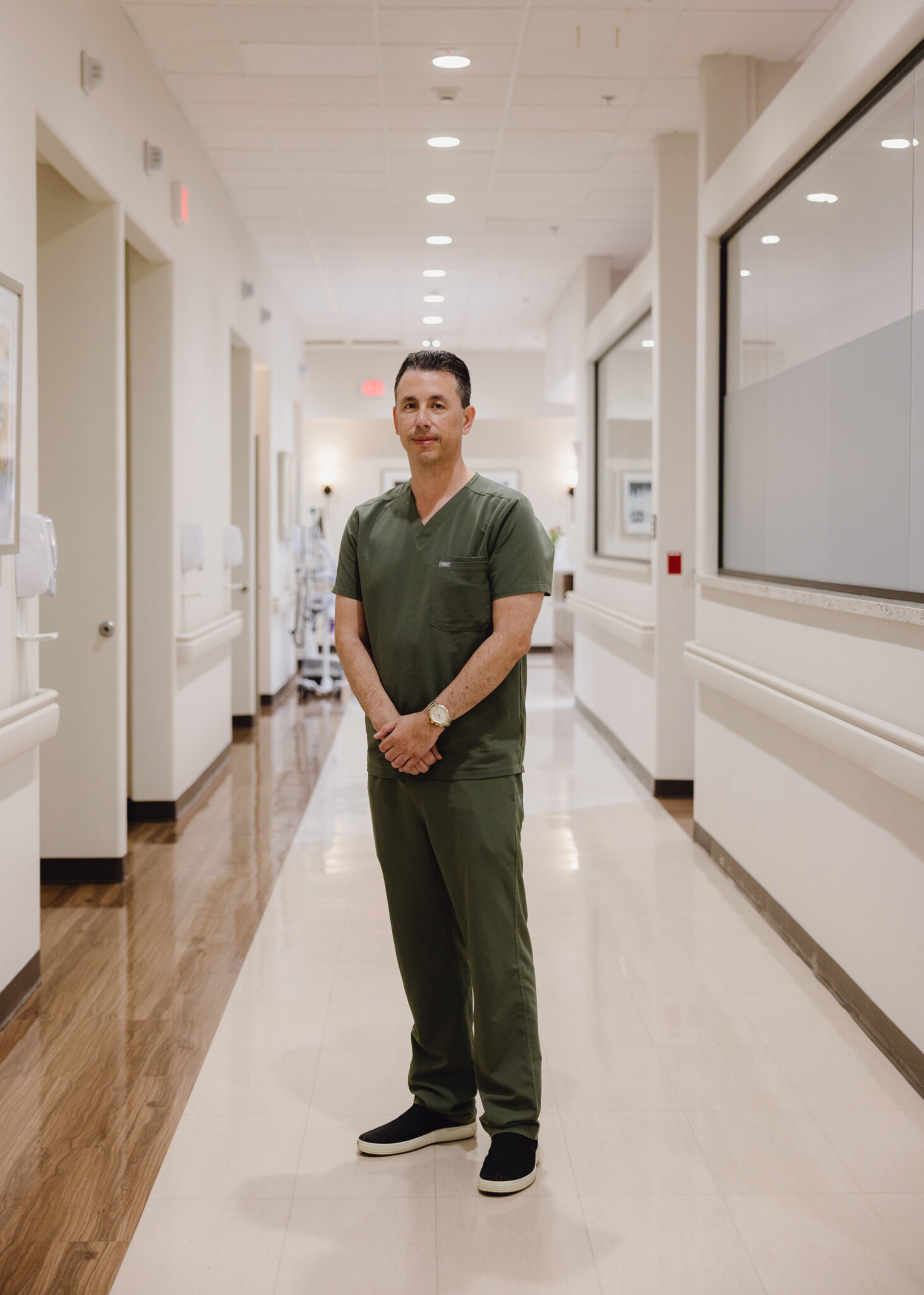 A man in green scrubs stands in a hospital hallway