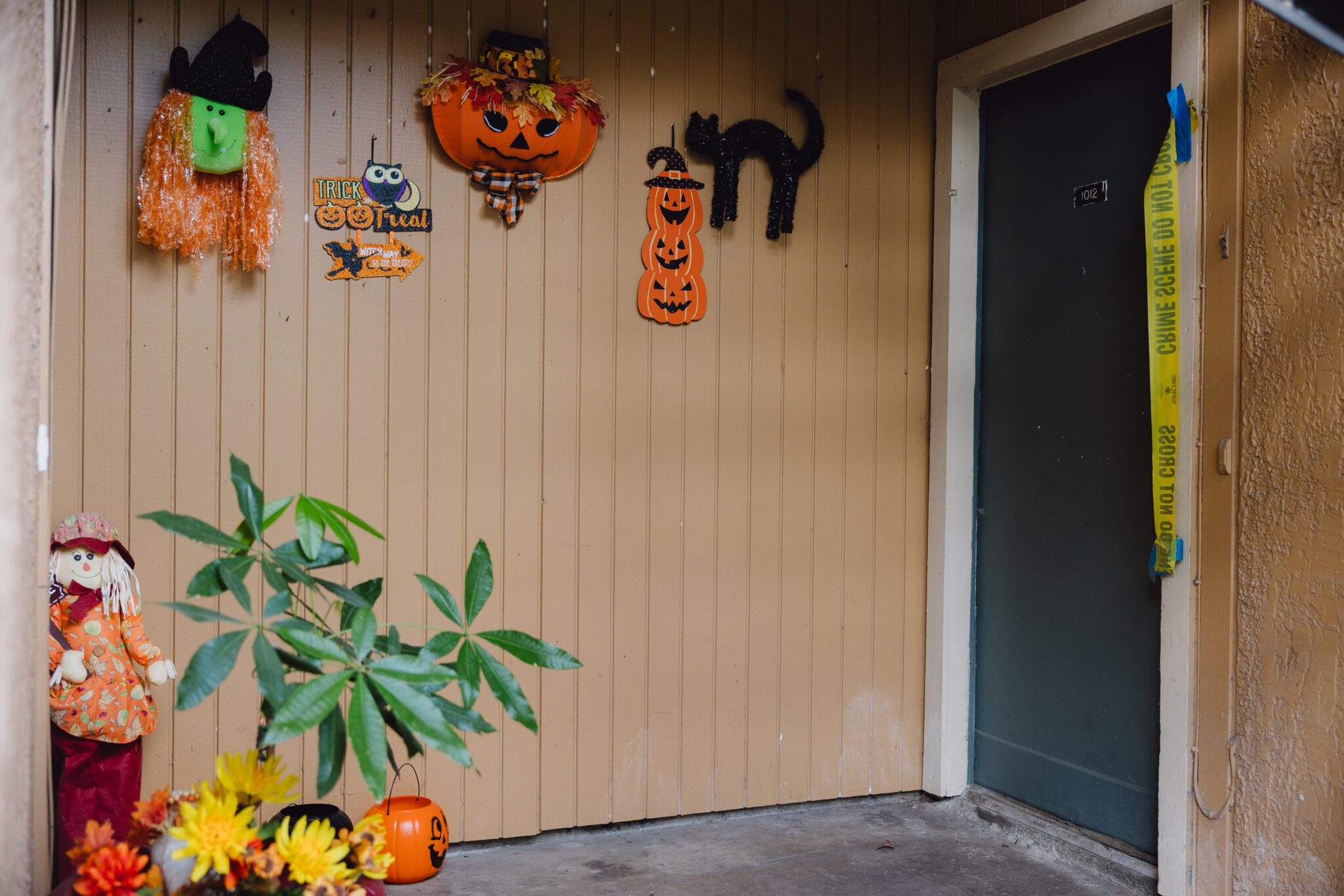 The entrance to an apartment is adorned with Halloween decorations while crime scene tape hangs next to the door