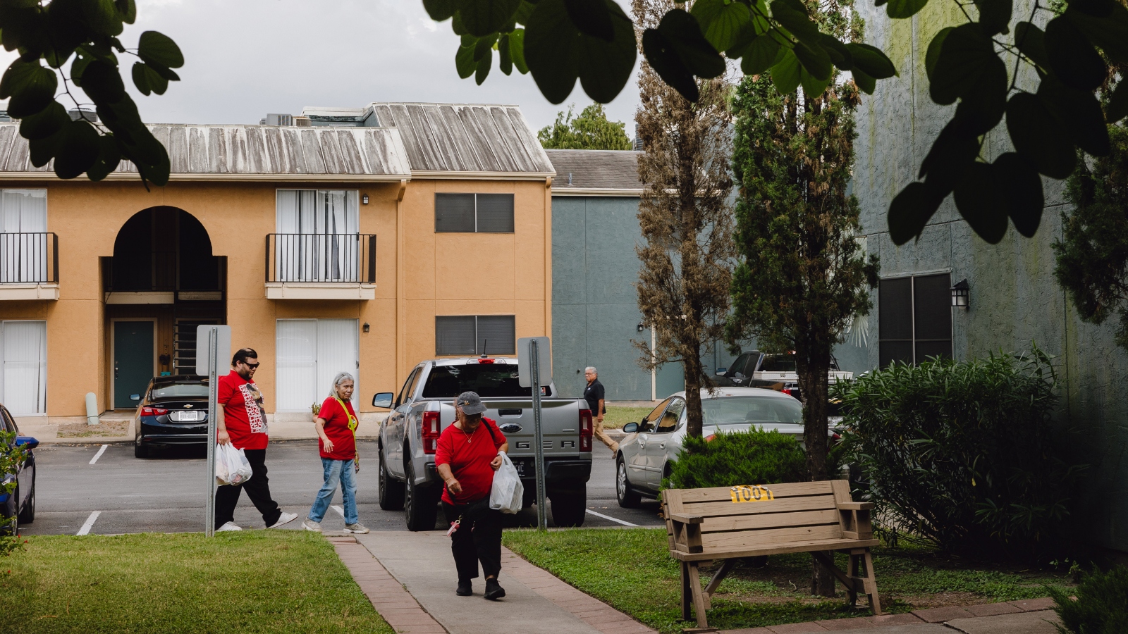 A group of people walk on a sidewalk in front of a two story apartment building