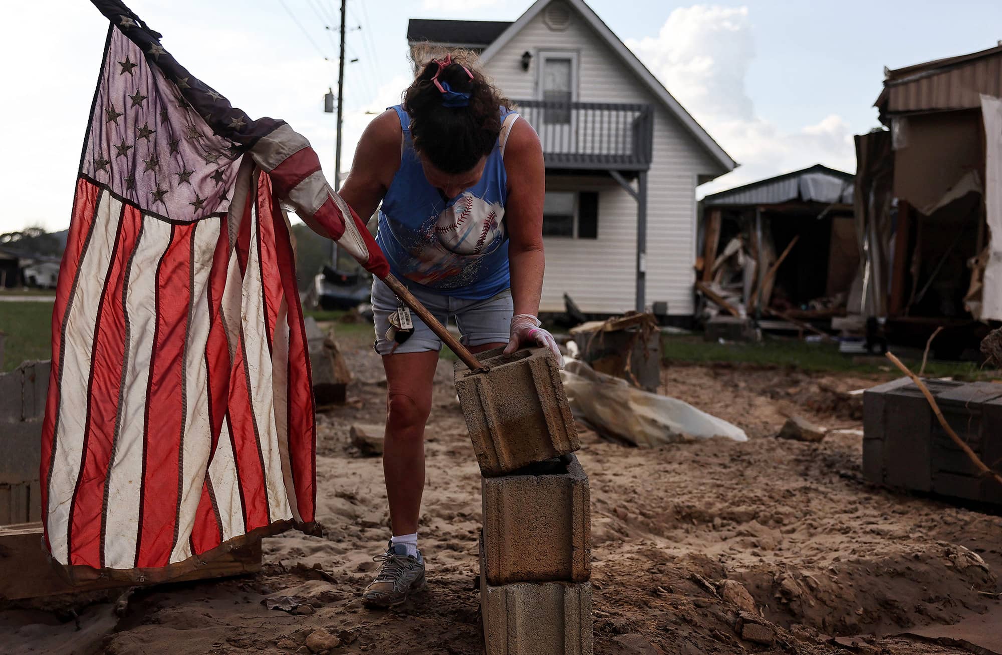 A woman mounts an American flag against a pile of cinder blocks outside her friend's destroyed garage (right) in the wake of Hurricane Helene flooding in Swannanoa, North Carolina.