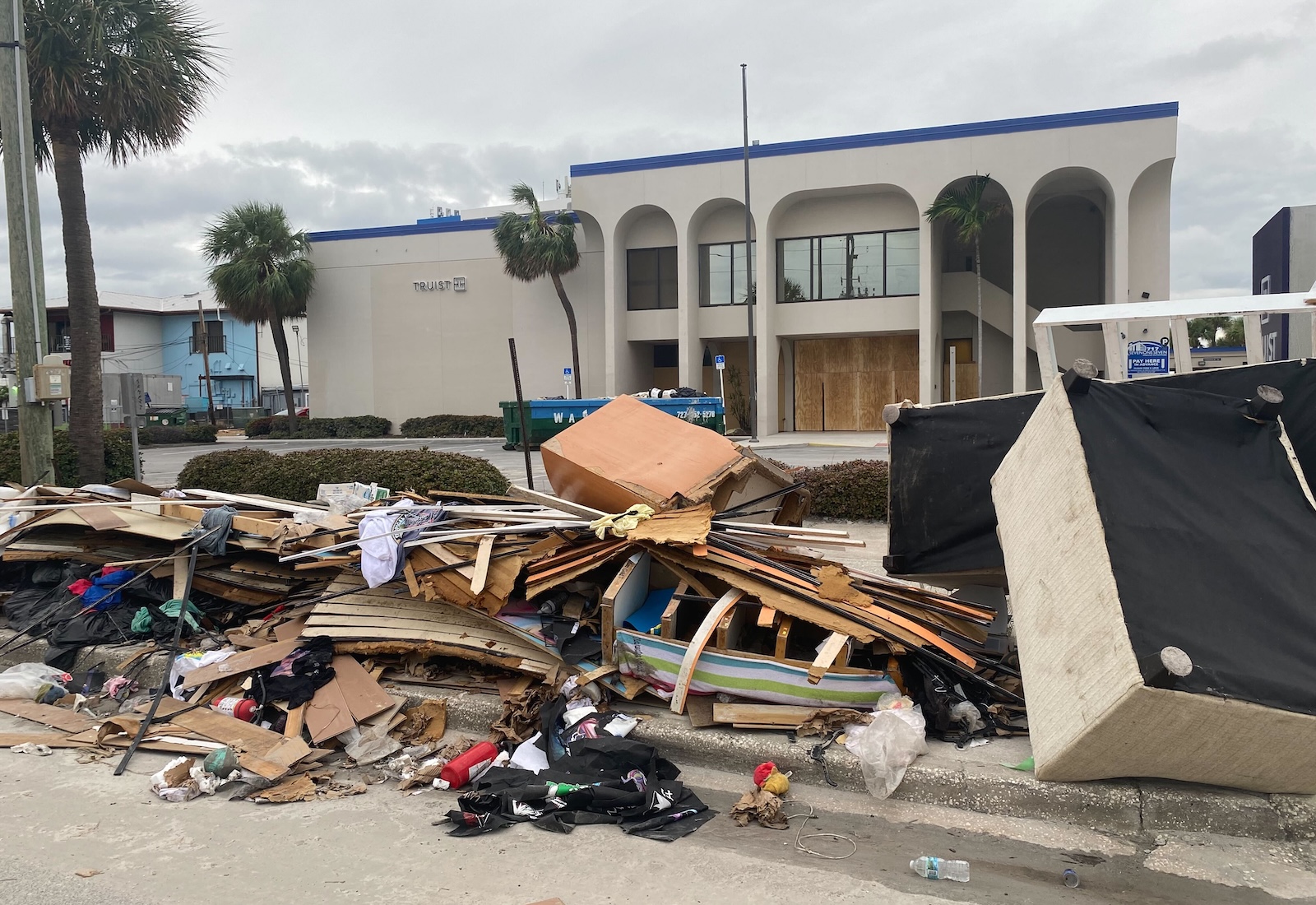 Debris and furniture piled up on the beach outside a building.