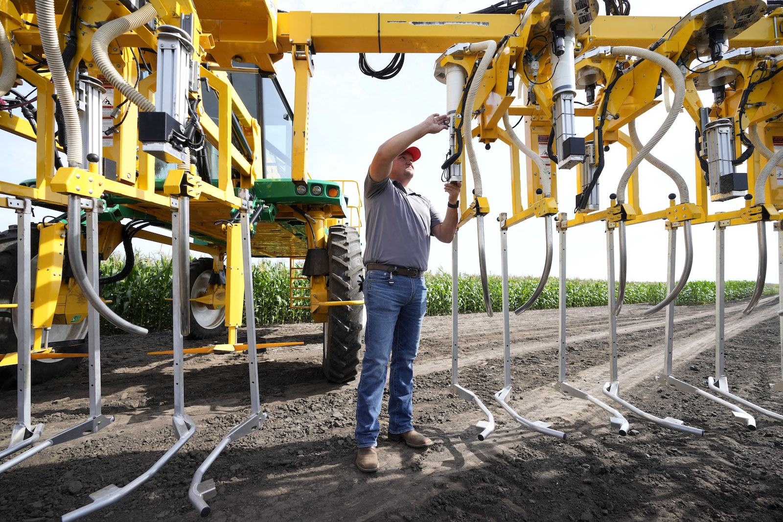 A man in a field reaches up to touch yellow farm equipment