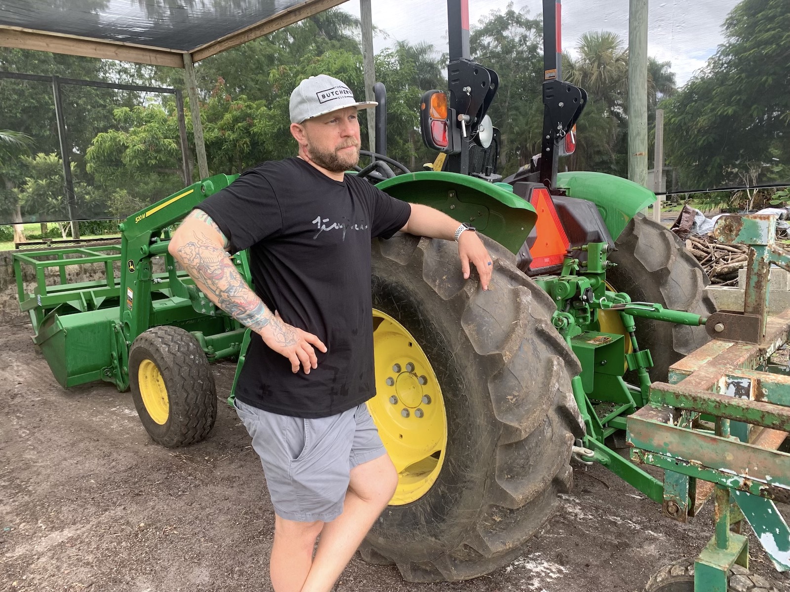 A man leans on the large wheel of a tractor with green paint