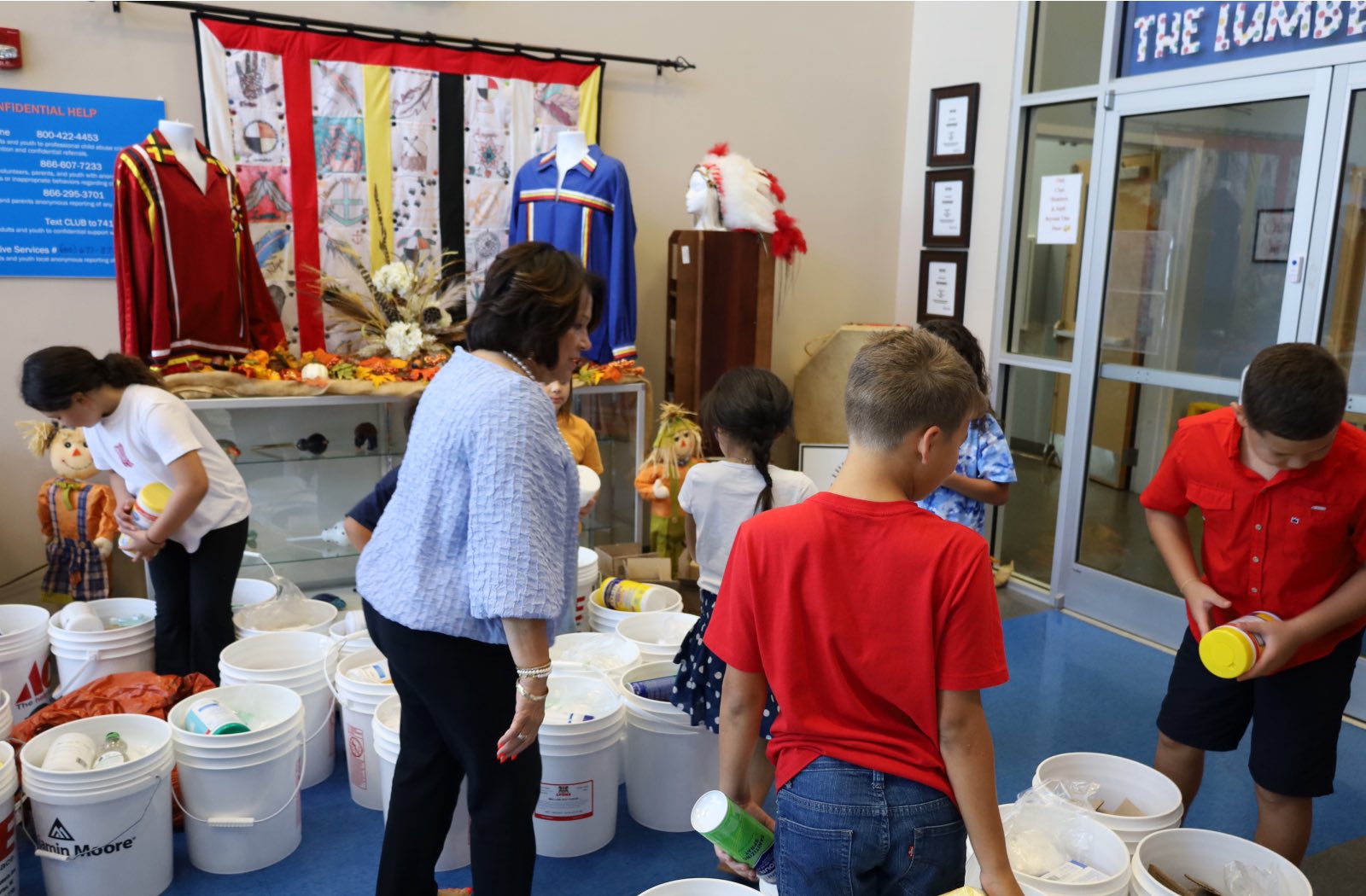 An elderly woman and three children stand in a room filled with buckets of supplies