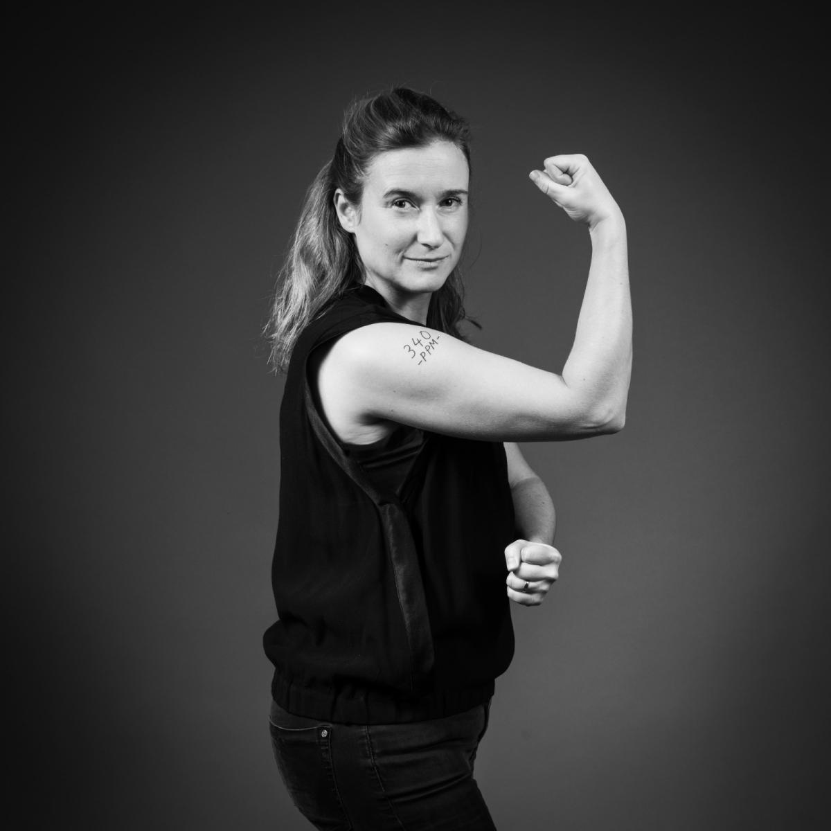 A woman with her arm raised into a fist, showing the 340 PPM tattooed on her bicep