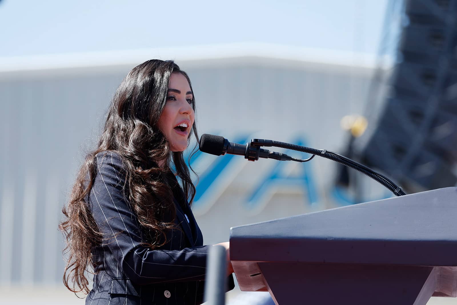 A woman in a suit speaks into a microphone at a podium