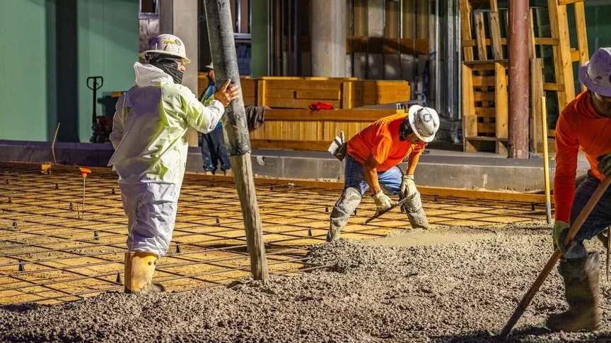 Two workers wearing hard hats spread concrete