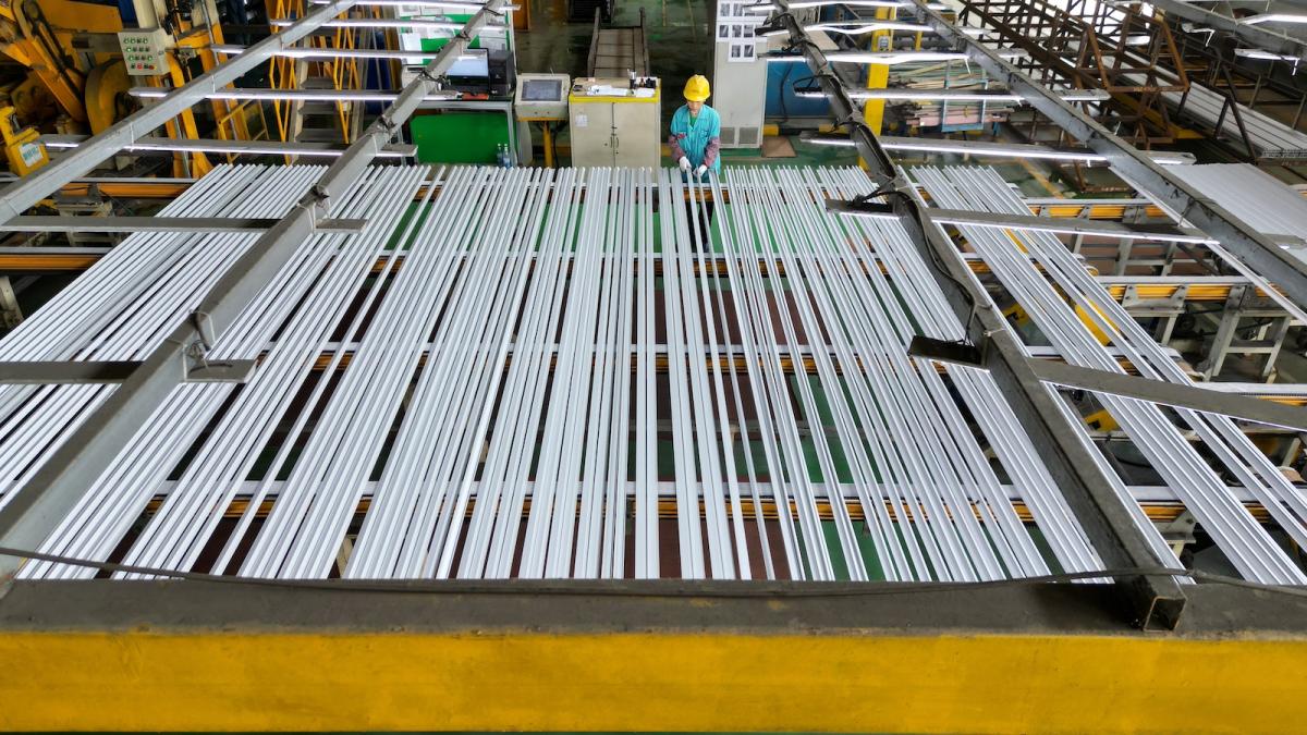 Overhead view of several silver metal strips sitting atop equipment, with a person wearing a green shirt and a yellow hard hat in the background