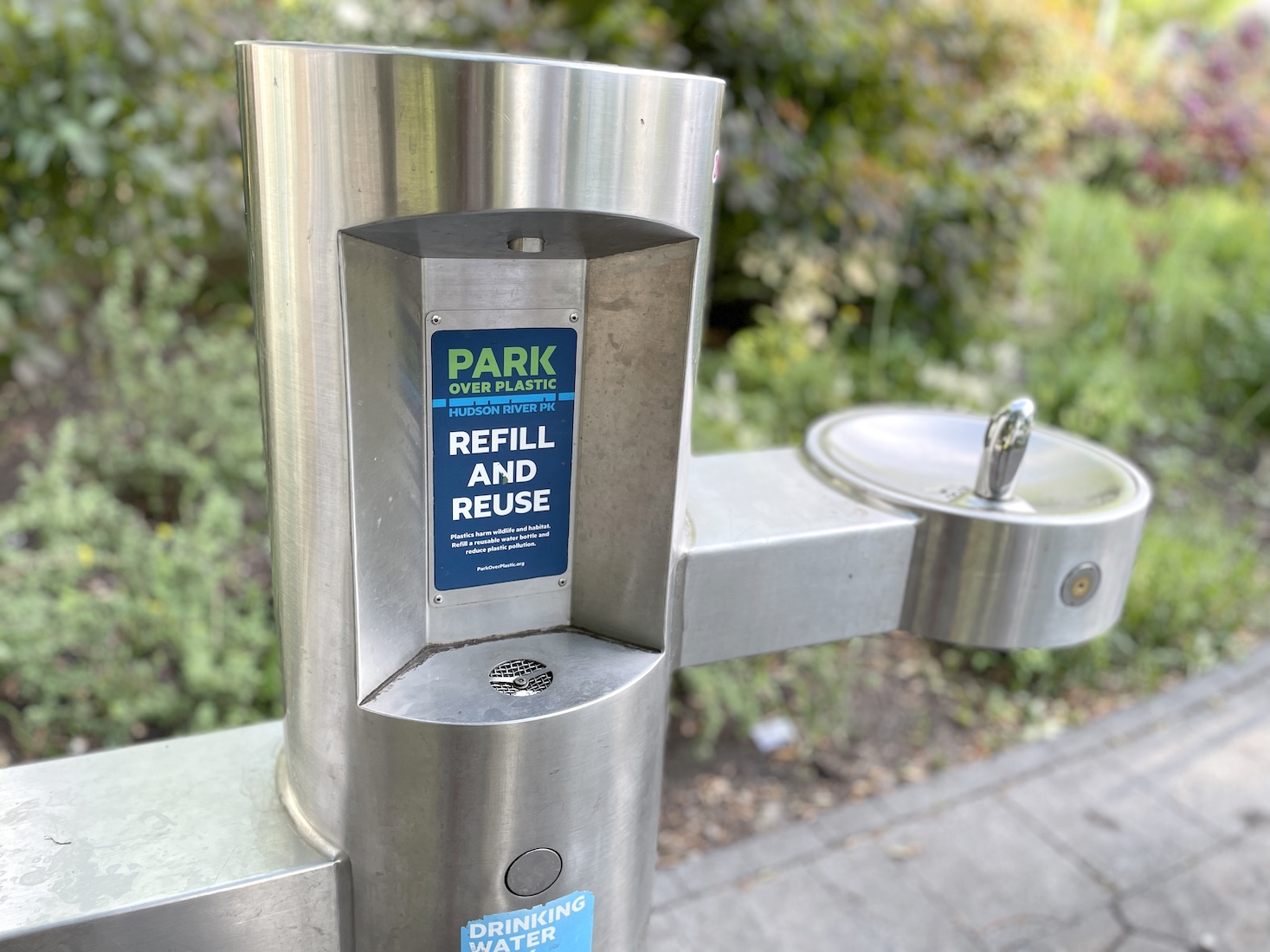 A refillable water station with a sign that reads "Parking over plastic: Refill and reuse."