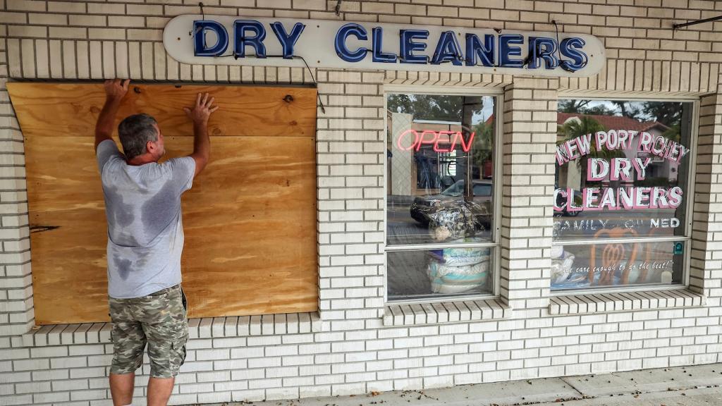 A man boards up the window of a dry cleaning business.