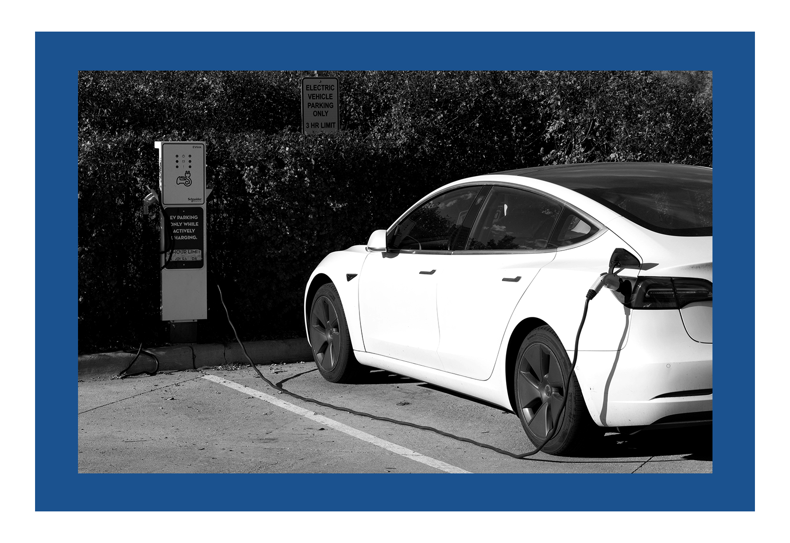 A black and white photo of an electric car plugged into a charger. The photo has a blue border around it