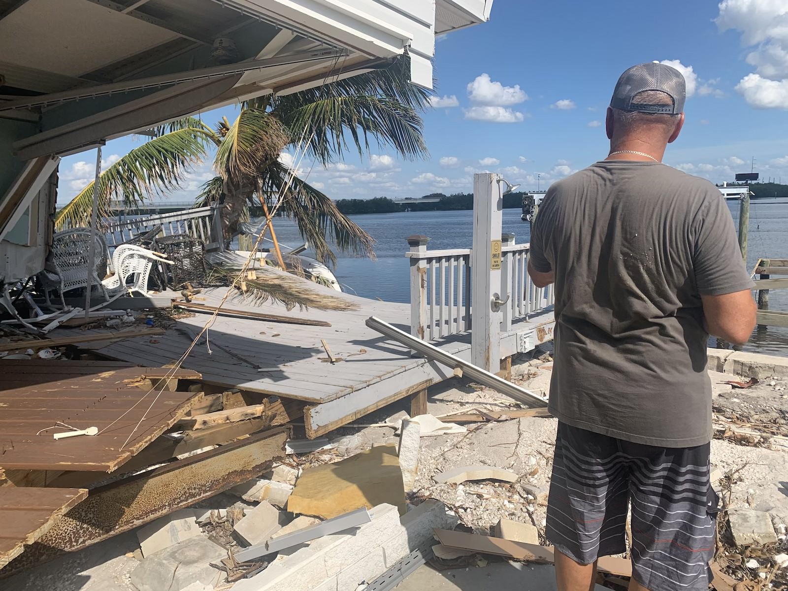 A man is looking at the remains of a house near the water