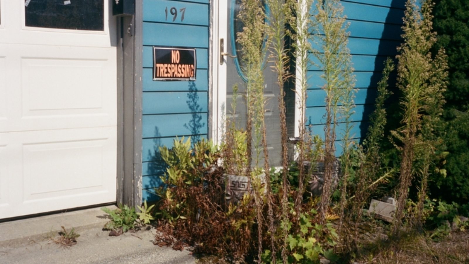 The front door of an abandoned blue house in Montpelier. There's a no trespassing sign pinned near the front door.