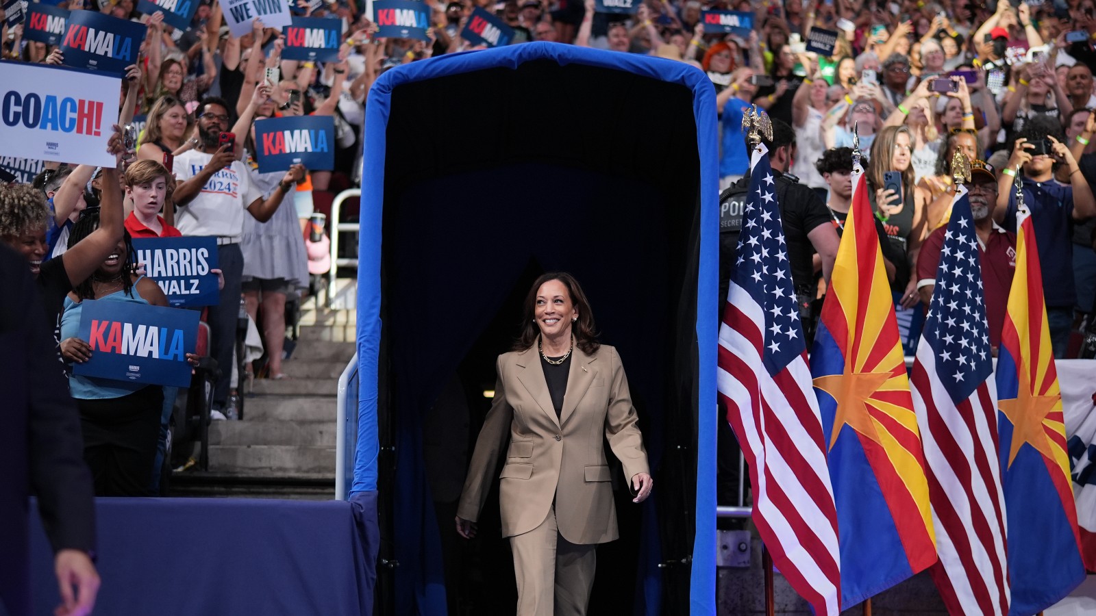 Kamala Harris walking on to a stage at a political rally, with spectators cheering behind her