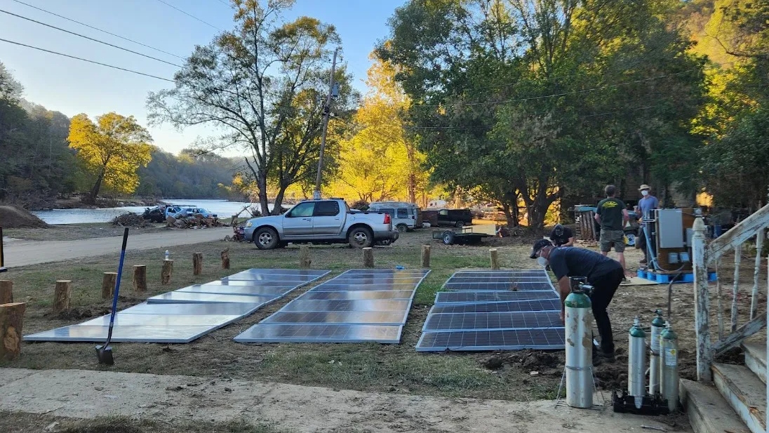 A series of solar panels are laid out on grass in front of cars