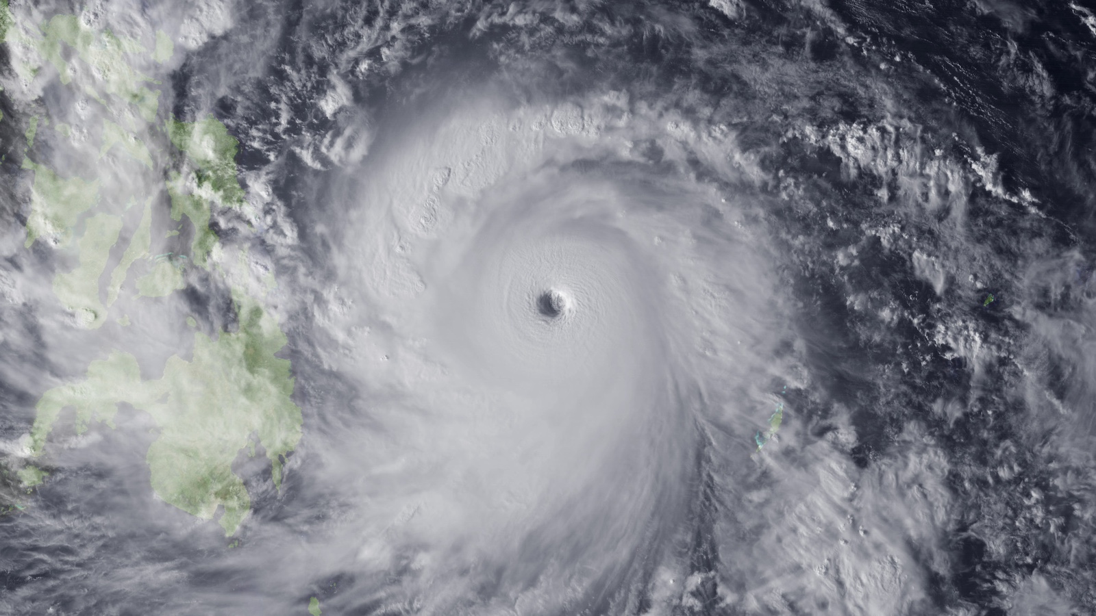 A satellite image of a massive white hurricane over a dark blue ocean and, to the right, the islands of the Philippines