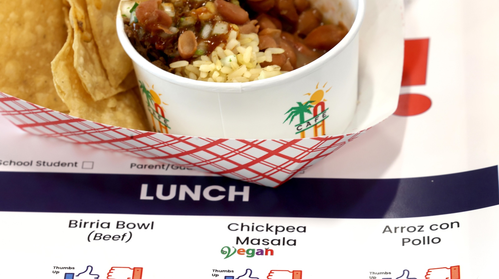 A close-up shot of a paper tray holding a bowl of rice and chickpeas; the paper tray is sitting on a larger plastic lunch tray that has a sheet on it where taste-testers can vote on the food items.