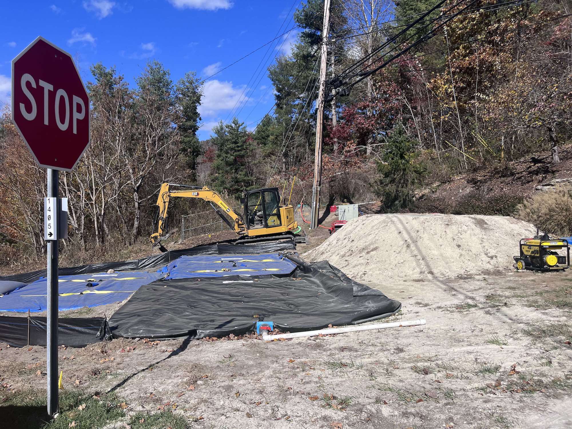 An excavator works near a black tarp and a stop sign