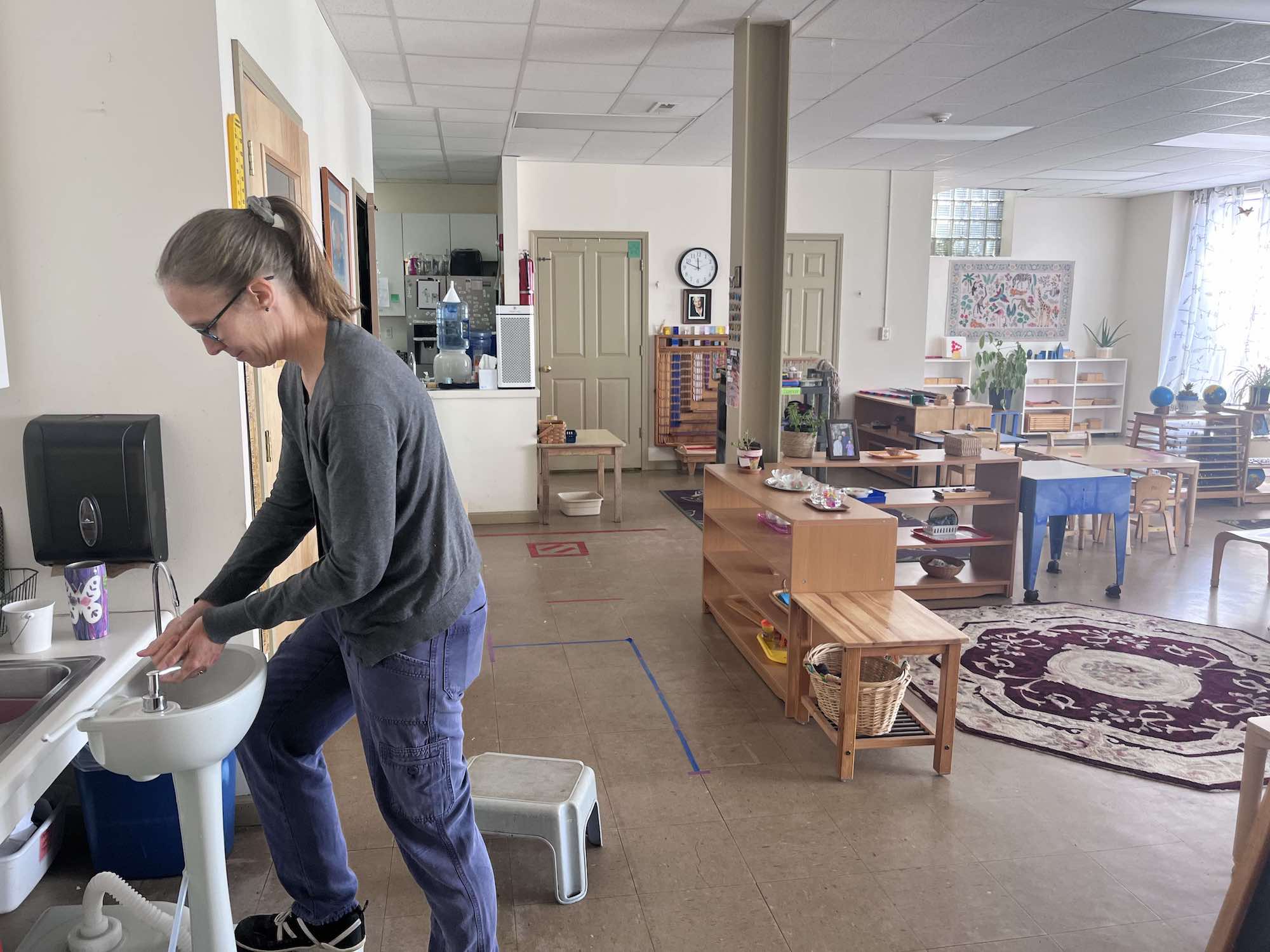 A woman with glasses washes her hands inside a large room