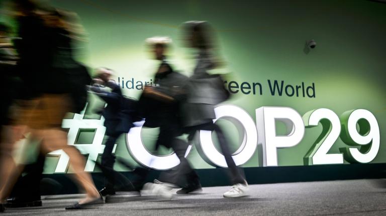 People walk past the logotype at the venue for the 2024 United Nations Climate Change Conference (COP29) in Baku on November 11, 2024.