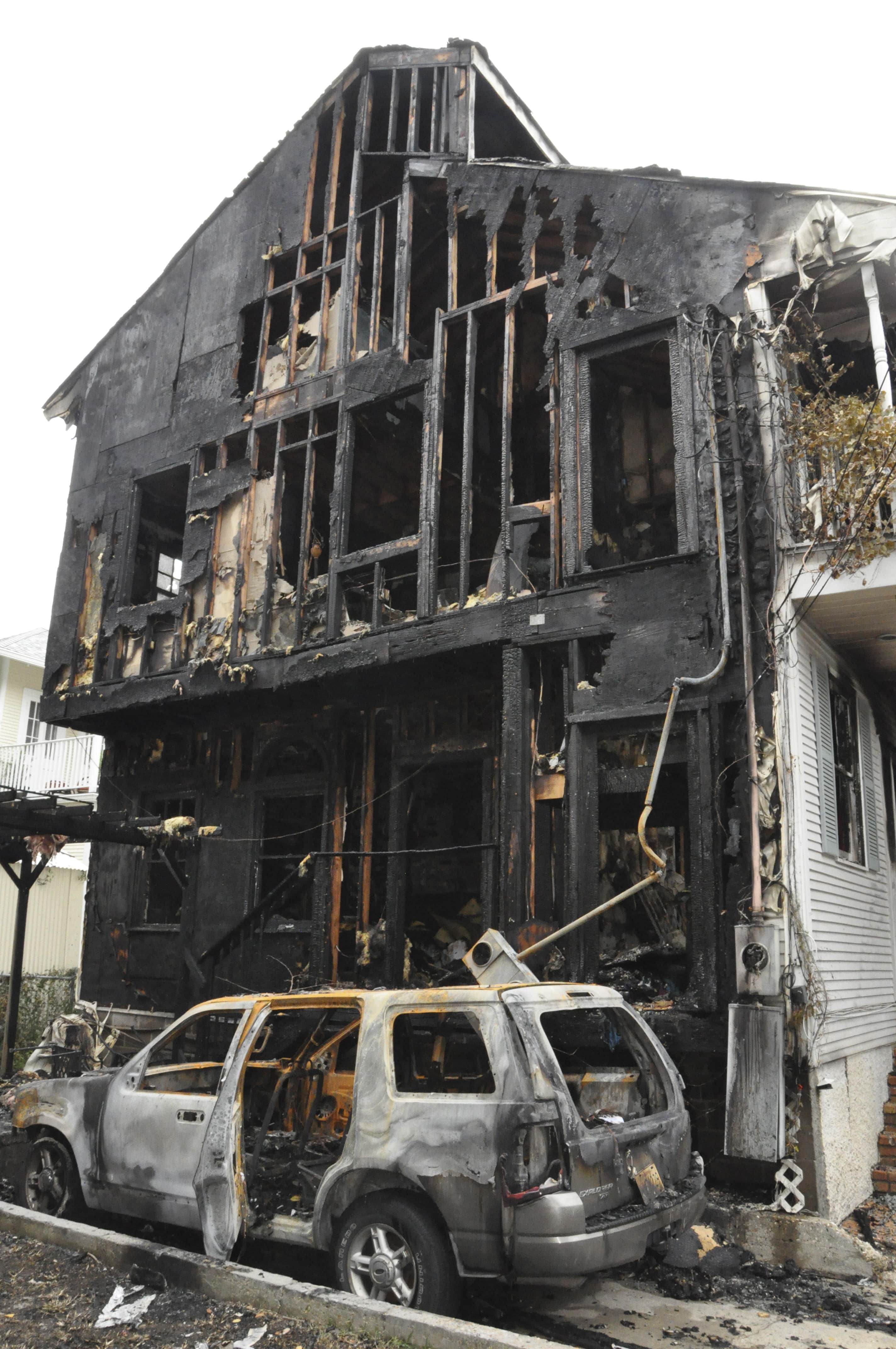 The charred remains of a house and car stand stark against a white sky