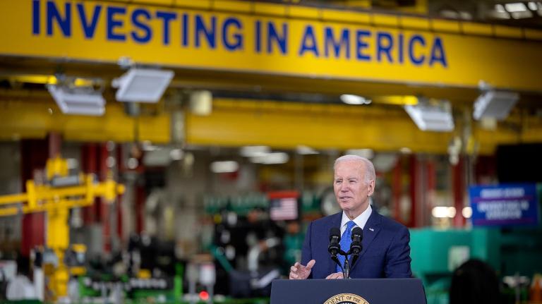 Joe Biden speaks at a podium in front of a sign that reads Investing in America