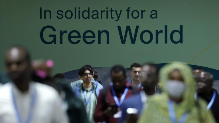 A group of people walk in front a banner that reads: 