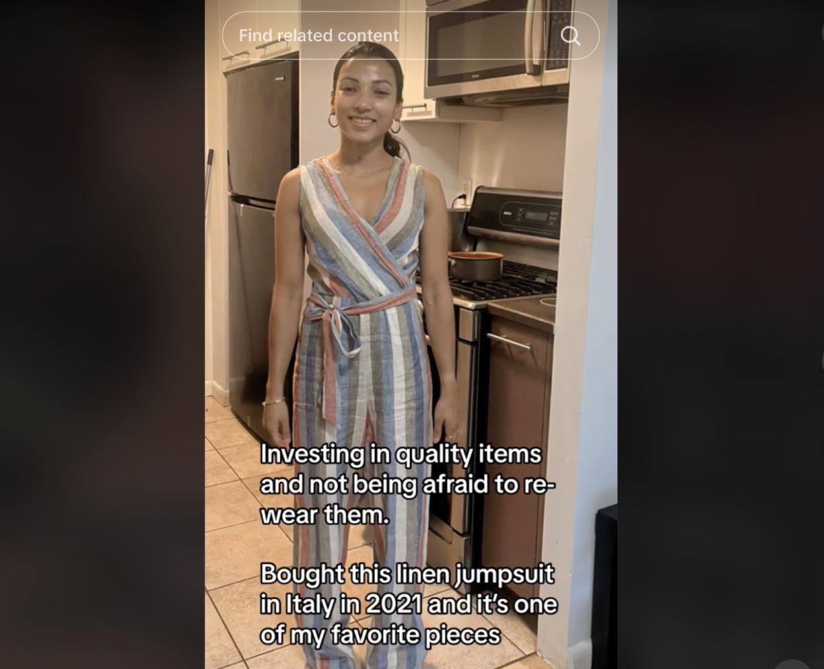 A photo of a woman standing in her kitchen wearing a striped linen jumpsuit and smiling