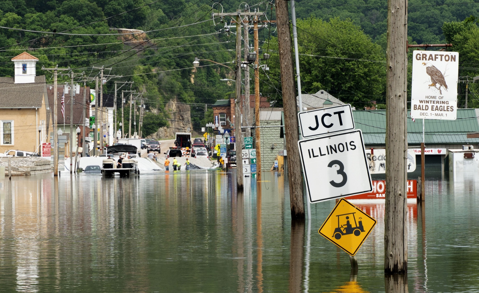 A sign that says Illinois 3 jct on a small town street is surrounded by flood waters