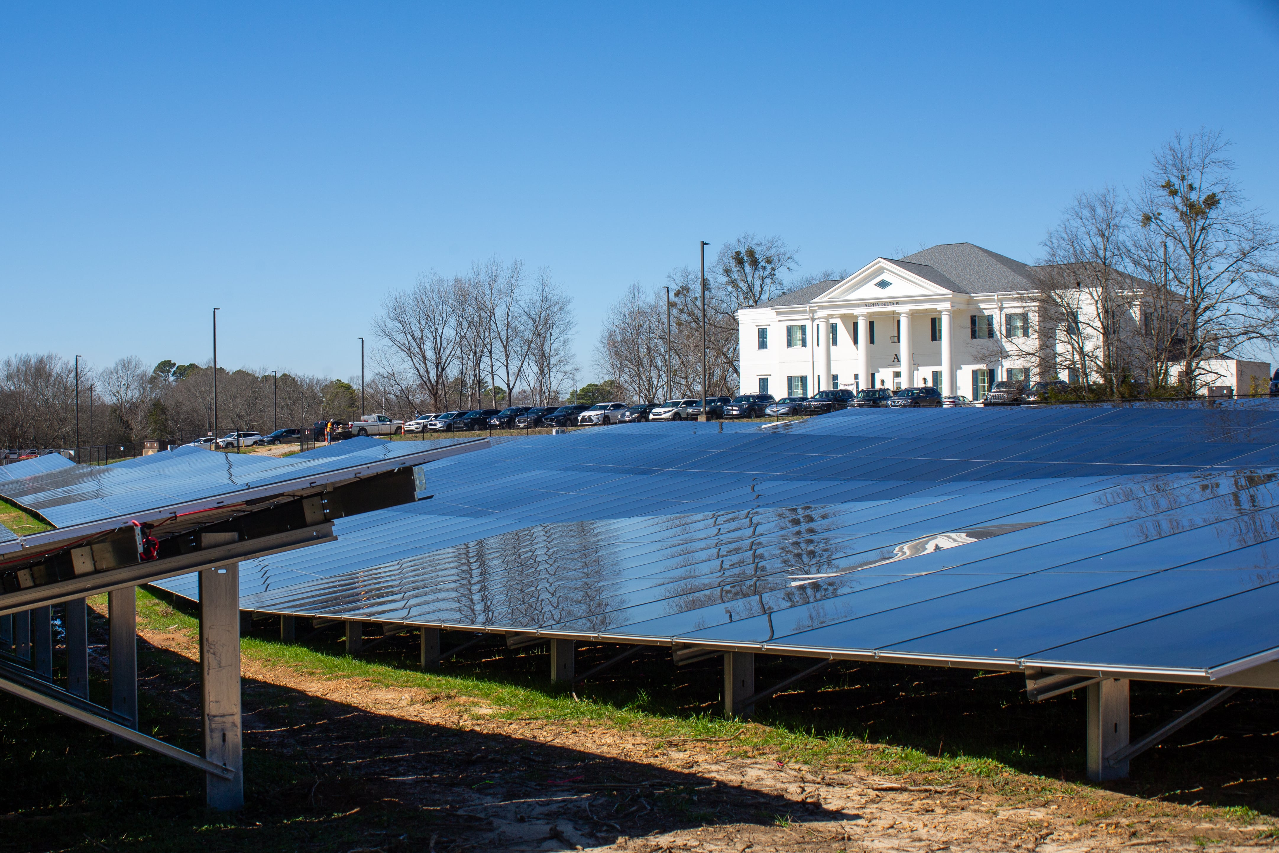 An array of solar panels on a field in front of a large white mansion