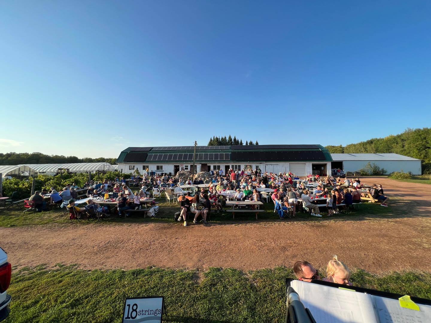 A crowd on a farm in front of a large white barn with solar panels