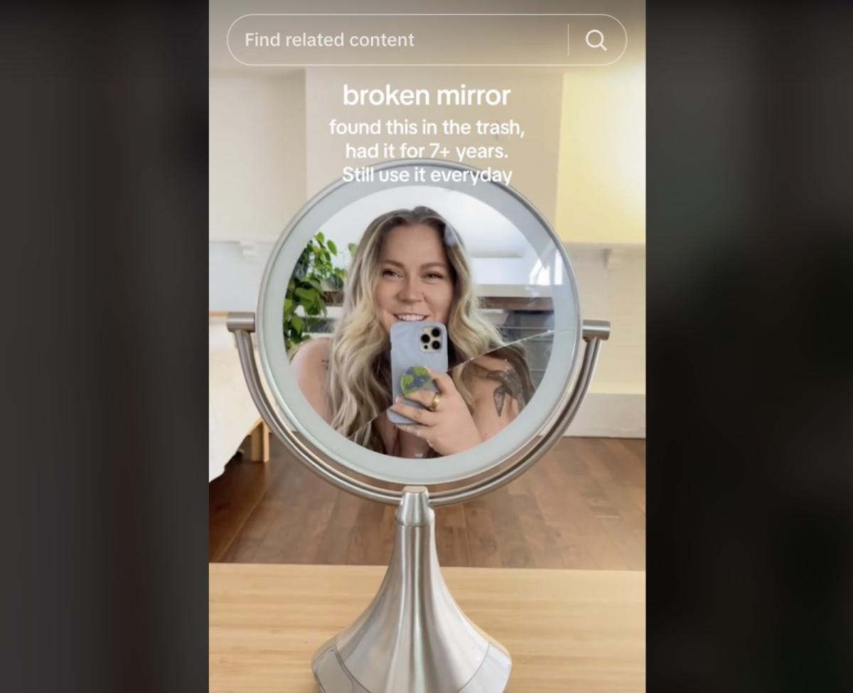 A photo of a woman smiling at her own reflection in a cracked mirror