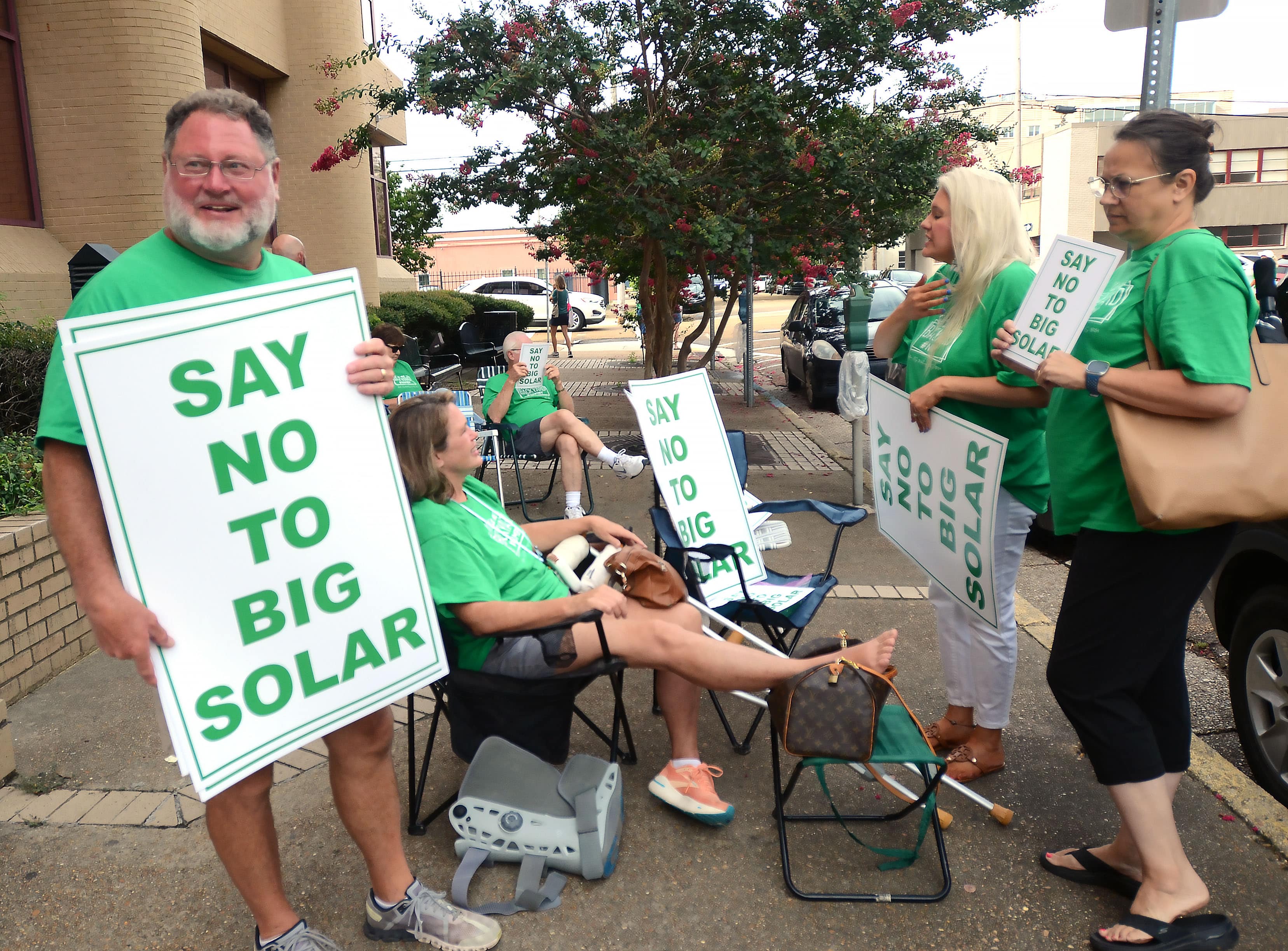 A group of people in green tee shirts hold signs saying Say No to Big Solar