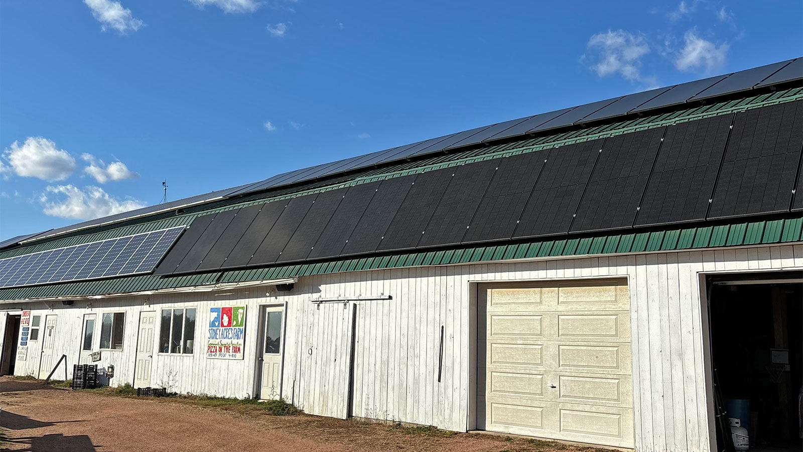 a wide white outbuilding on a farm with many solar panels on the roof