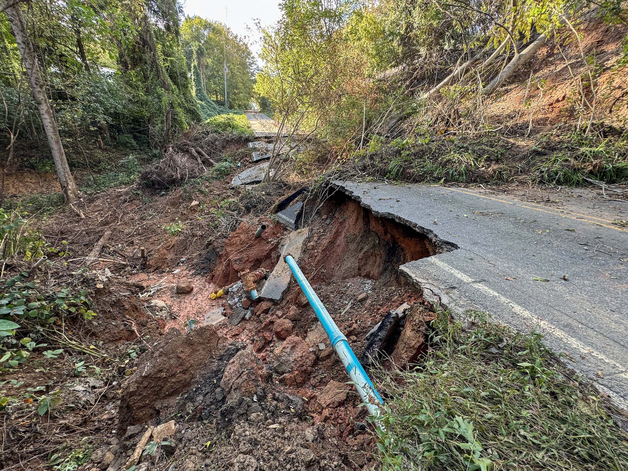 A pipe runs in the exposed gap underneath a damaged road