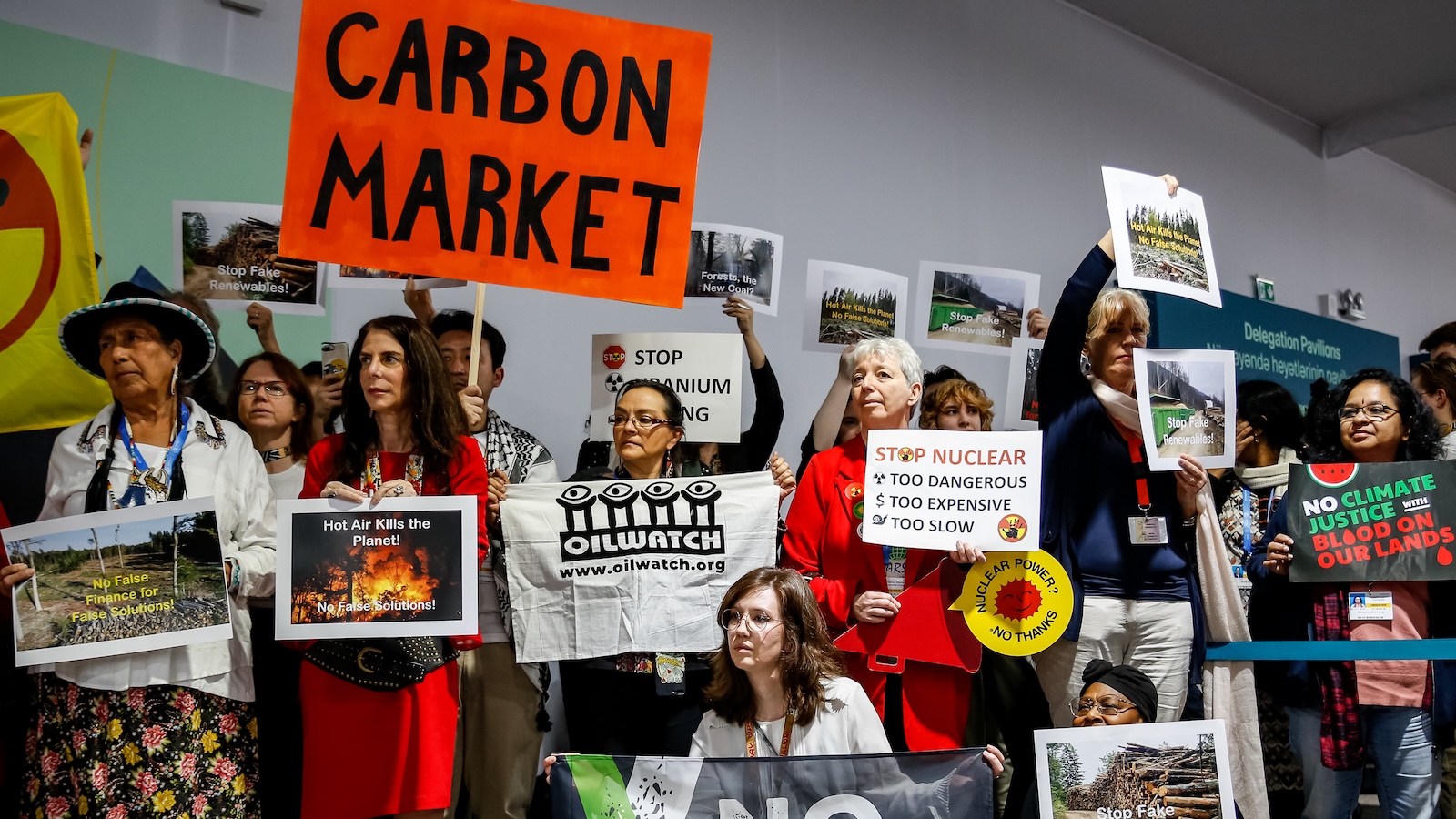 Protesters hold signs, including a prominent red one reading "carbon market"